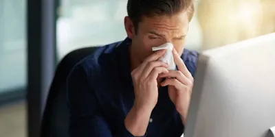 Un homme éternue vers son ordinateur, il est à la recherche de la période d'incubation du rhume