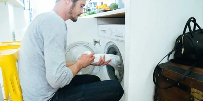 Mies laittaa vaatteita pesukoneeseen